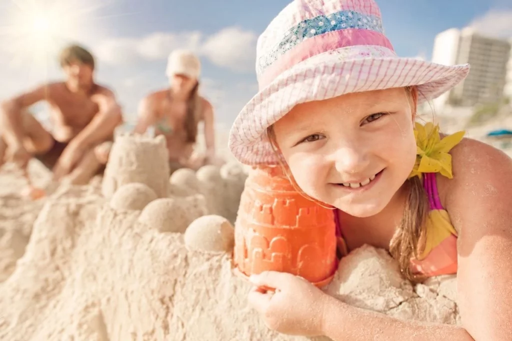 Een kind kijkt blij in de camera op het strand, terwijl op de achtergrond twee volwassenen onscherp zichtbaar zijn. Het beeld benadrukt hoe belangrijk rust, veiligheid en ruimte om kind te zijn zijn, ook wanneer ouders uit elkaar gaan.