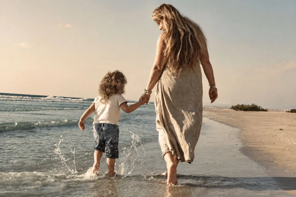 Moeder kijkt naar haar kind terwijl ze samen door het water langs het strand lopen.